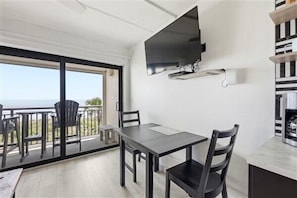 A balcony with a table and chairs, a TV mounted on the wall, and a view of the sea.