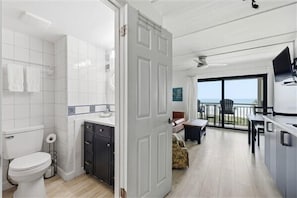 A modern kitchen with a dining area, a large sliding glass door leading to a balcony, and a visible toilet.