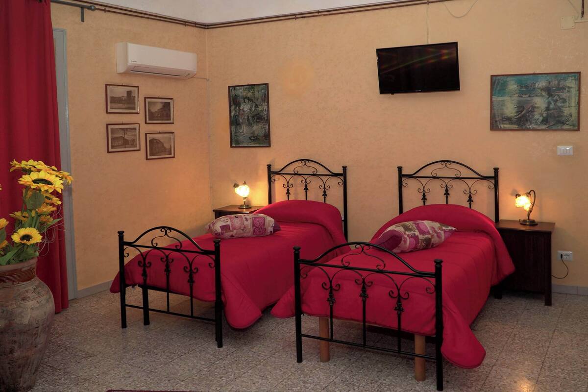 A bedroom with two beds, a red curtain, a vase with flowers, and wall-mounted artwork.