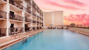 Un hotel de varios pisos con piscina, balcones y tumbonas.