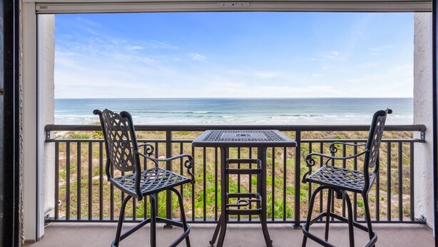 Een balkon met twee metalen stoelen en een kleine tafel, met uitzicht op de oceaan.