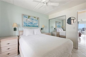 A bedroom with a bed, nightstands, a ceiling fan, a painting, a mirror, and a view of the balcony. - Beacher's Oceanfront Balcony Suite with Onsite Front desk and staff (St. Augustine)