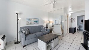 A modern living room with a grey sofa, a coffee table, a floor lamp, and a ceiling fan. - Beacher's Oceanfront Balcony Suite with Onsite Front desk and staff (St. Augustine)