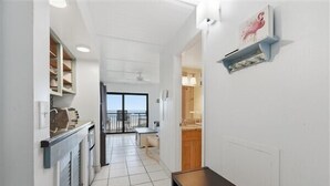 A narrow hallway with a dining area at the end, a kitchen with a built-in oven, and a view through a glass door to an outdoor balcony. - Beacher's Oceanfront Balcony Suite with Onsite Front desk and staff (St. Augustine)