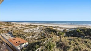 A beach view with a sandy path leading to the shore, a wooden fence, and a building with a red roof. - Beacher's Oceanfront Balcony Suite with Onsite Front desk and staff (St. Augustine)