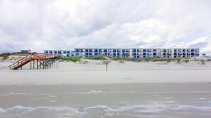 A beachfront hotel with a pier, multiple balconies, and a sandy beach.