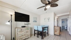 A dining area with a ceiling fan, a TV mounted on the wall, and a rustic wooden cabinet.