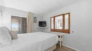Une chambre à coucher avec un lit, une télévision, un miroir et une fenêtre avec des rideaux.