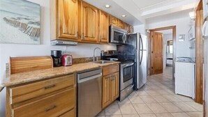 A kitchen with wooden cabinets, stainless steel appliances, and a tiled floor. - Beacher's Oceanfront Balcony Suite with Onsite Front desk and staff (St. Augustine)