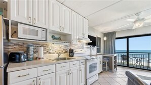 A modern kitchen with white cabinets, a microwave, and a stove. There is a balcony with a view of the ocean.