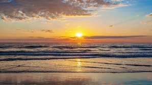 A beach with waves and a sunset.