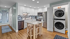 A modern kitchen with white cabinets, a granite countertop, stainless steel appliances, and a double-door washer and dryer.