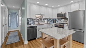 A modern kitchen with white cabinets, a granite countertop, stainless steel appliances, and a tiled backsplash.