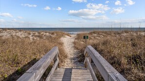 A wooden boardwalk leading to a beach with a clear sky and distant ocean.
