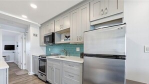 A modern kitchen with white cabinets, a stainless steel refrigerator, a microwave, and an oven. - Beacher's Oceanfront Balcony Suite with Onsite Front desk and staff (St. Augustine)