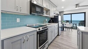 A modern kitchen with white cabinets, a black microwave, a stove, and a sink. There is a balcony with a table and chairs. - Beacher's Oceanfront Balcony Suite with Onsite Front desk and staff (St. Augustine)