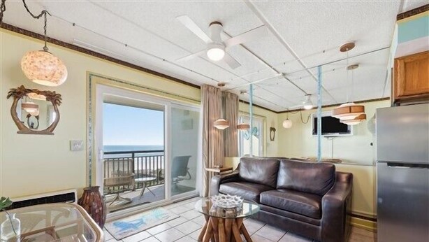 A living room with a leather sofa, a glass coffee table, and a dining table with chairs. There is a balcony with a view of the sky. - Beacher's Oceanfront Balcony Suite with Onsite Front desk and staff (St. Augustine)