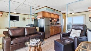 A modern living room with leather sofas, a glass coffee table, and a kitchen area with wooden cabinets and stainless steel appliances. - Beacher's Oceanfront Balcony Suite with Onsite Front desk and staff (St. Augustine)
