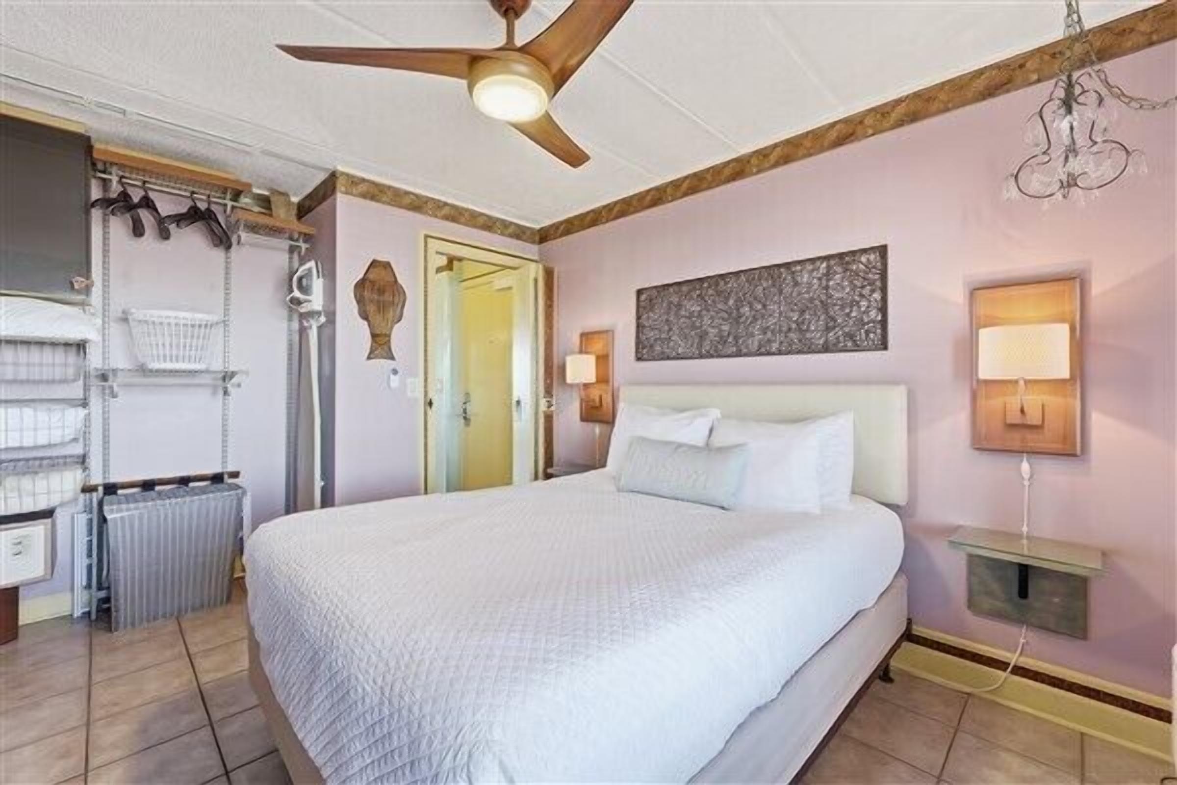 A bedroom with a bed, ceiling fan, wall-mounted lamps, and a radiator.