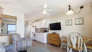 A living room with a sofa, a dining table with chairs, a TV, and a kitchen area.