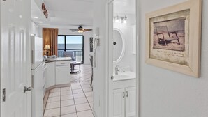 A hotel room with a kitchen area, a bathroom with a framed picture, and a view of the ocean through a window. - Beacher's Oceanfront Balcony Suite with Onsite Front desk and staff (St. Augustine)