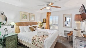 A well-lit bedroom with a bed, a ceiling fan, a nightstand with a lamp, a dresser, and a mirror. - Beacher's Oceanfront Balcony Suite with Onsite Front desk and staff (St. Augustine)
