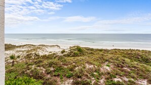 A beach view with a grassy foreground and a clear sky.