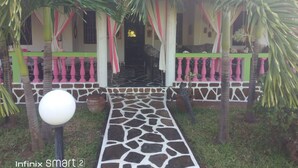 A building with a stone pathway leading to a door, surrounded by palm trees and a thatched roof structure. - Nuru Ya Erika Villas (Malindi)
