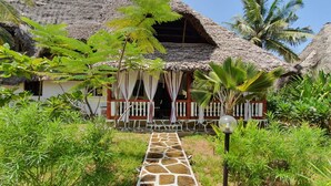 A thatched-roof house with a stone pathway leading to the entrance, surrounded by tropical vegetation. - Nuru Ya Erika Villas (Malindi)