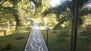 A stone pathway in a garden with palm trees and a stone wall in the background. - Nuru Ya Erika Villas (Malindi)