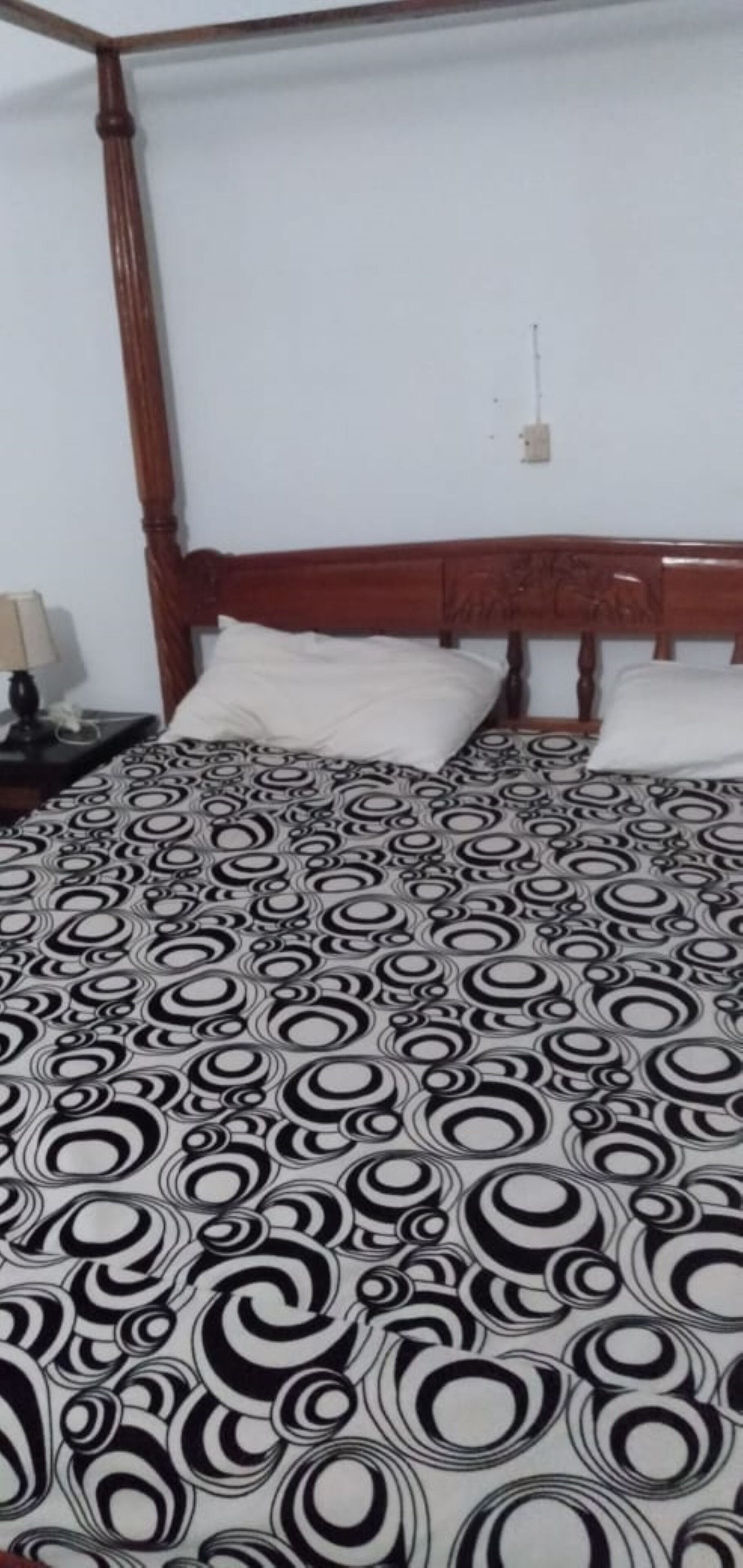 A bed with a patterned bedspread, a wooden headboard, and a nightstand with a lamp.