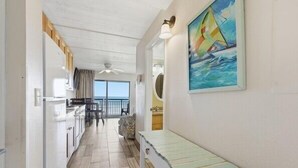 A narrow hallway with a kitchen area on the left, a dining area with a table and chairs, and a bench on the right. - Your New Favorite Beachside Escape | Top Floor & Oceanfront (St. Augustine)