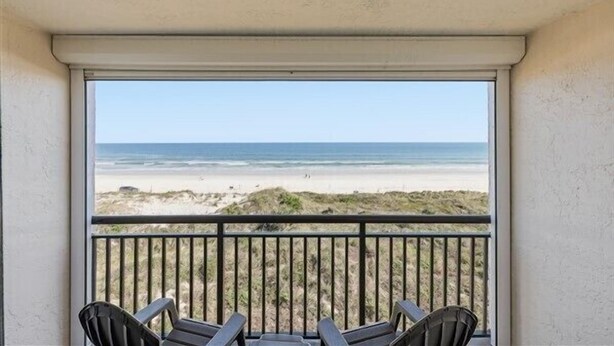 A balcony with a view of the beach, featuring two chairs and a table. - Your New Favorite Beachside Escape | Top Floor & Oceanfront (St. Augustine)