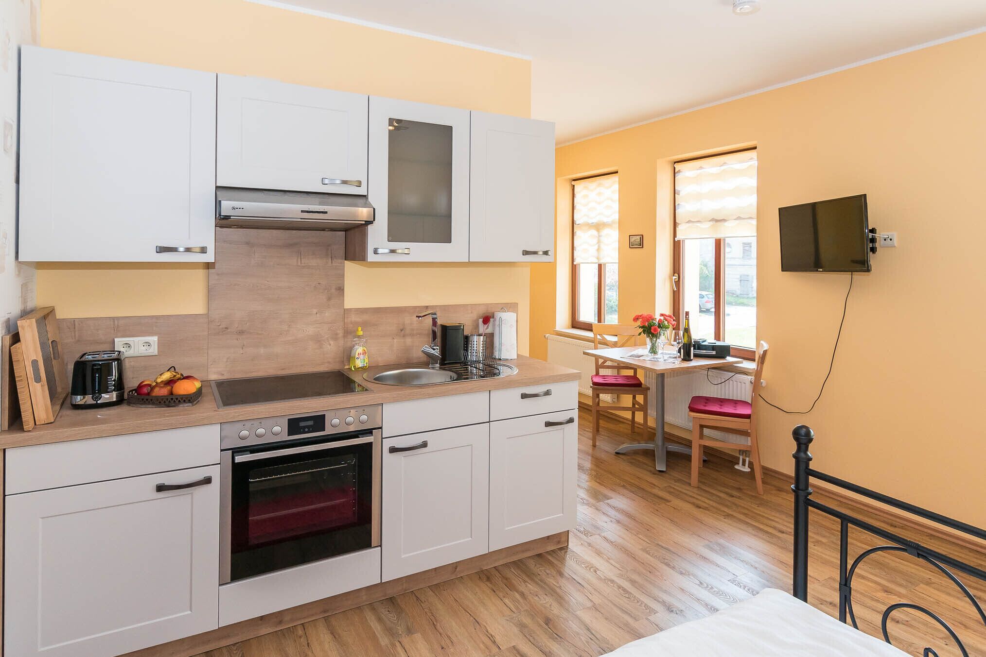 A compact kitchen with white cabinets, a built-in oven, and a window with blinds.