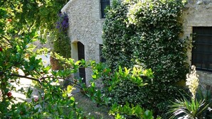 A stone building with a garden, featuring a large bush with white flowers, a small tree with red fruits, and a cactus. - Solimago Dimora Storica (Solferino)
