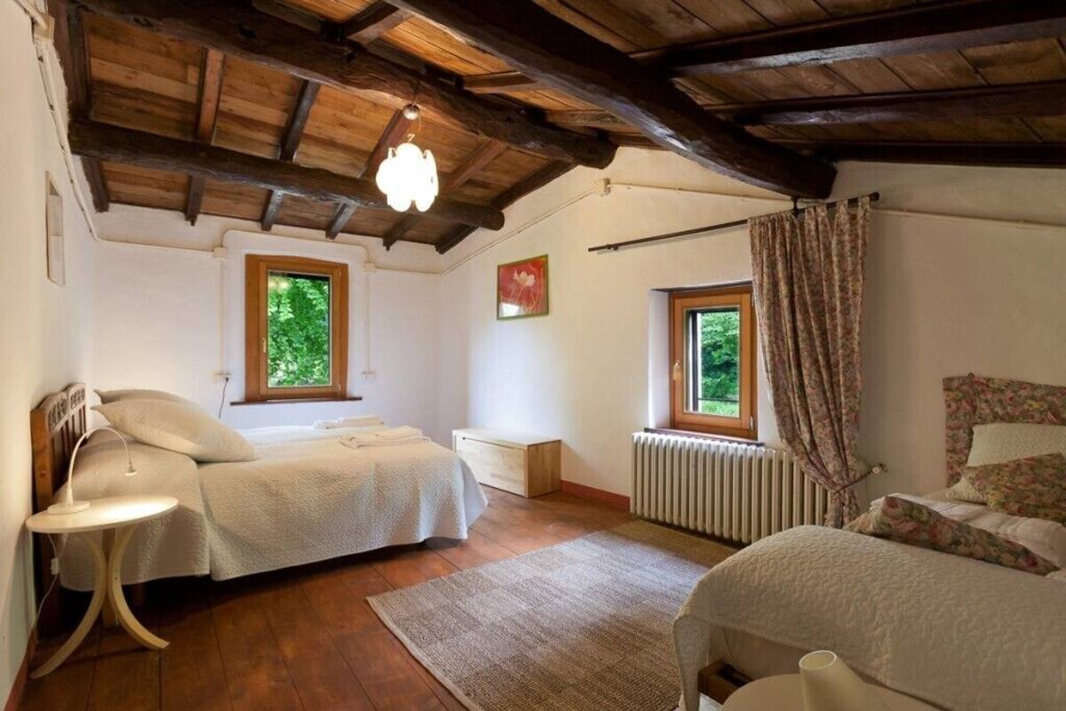 A cozy bedroom with a wooden ceiling, two beds, a radiator, and a window with curtains.