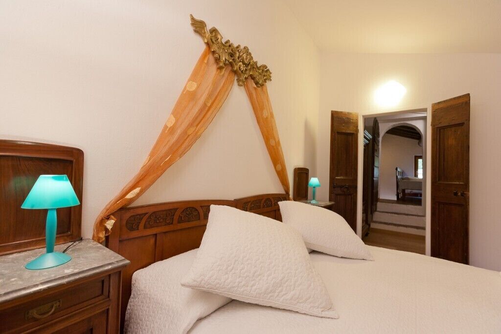 Un dormitorio con cabecera de madera, cama con ropa blanca y mesita de noche con lámpara.