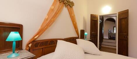 Un dormitorio con cabecera de madera, cama con ropa blanca y mesita de noche con lámpara.