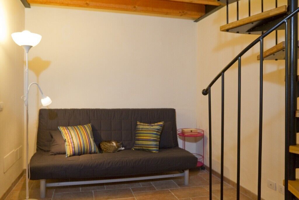 A dark-colored sofa with striped and solid pillows, a floor lamp, and a small pink side table with a red object.