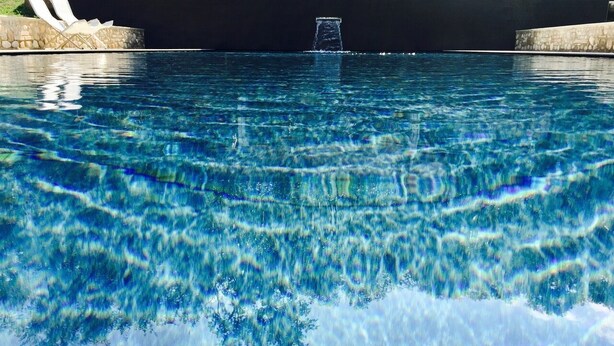 A clear swimming pool with a stone border and a single water fountain in the center. - Solimago Dimora Storica (Solferino)