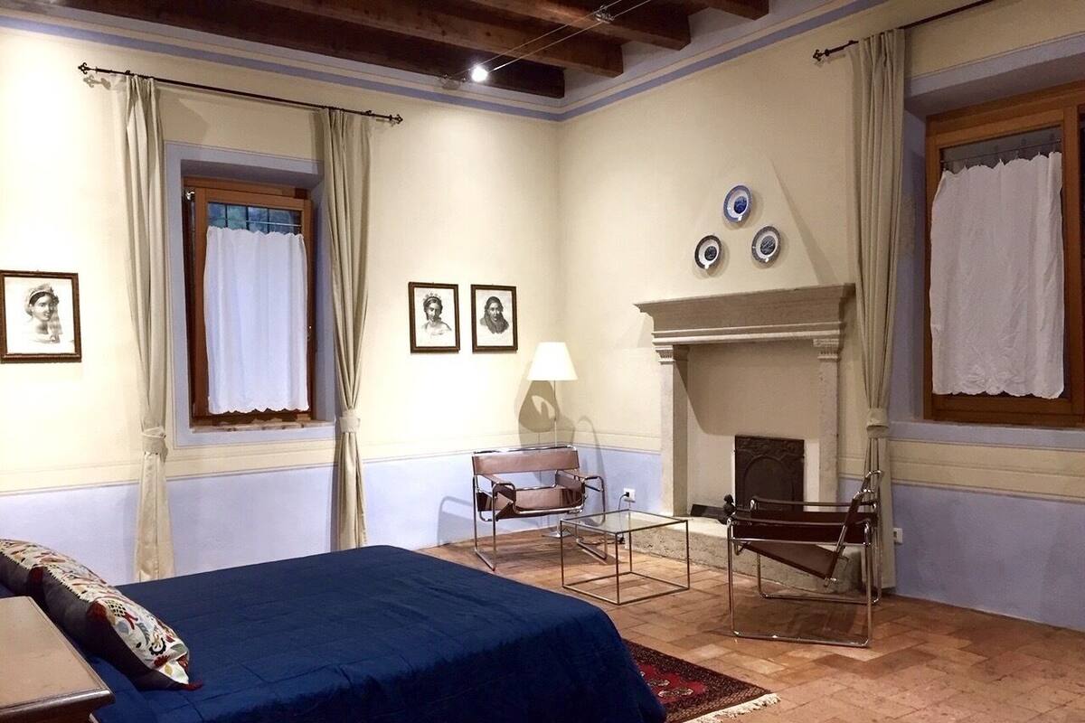A bedroom with a bed, a chair, a lamp, and a fireplace.