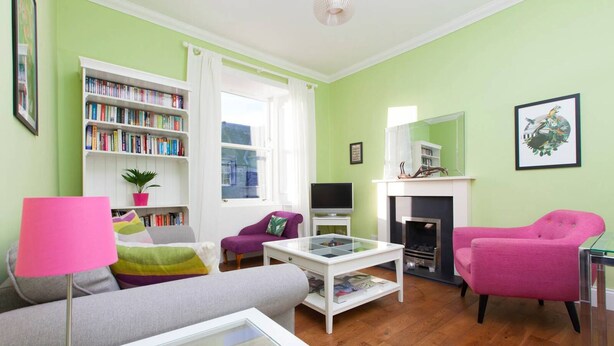 A living room with a sofa, armchair, coffee table, bookshelf, fireplace, and a television.