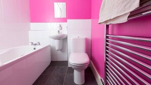 A bathroom with a pink wall, white tiles, a white bathtub, a white toilet, and a white sink.