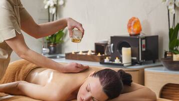A person receiving a massage in a spa setting with a massage table, candles, and a salt lamp in the background.