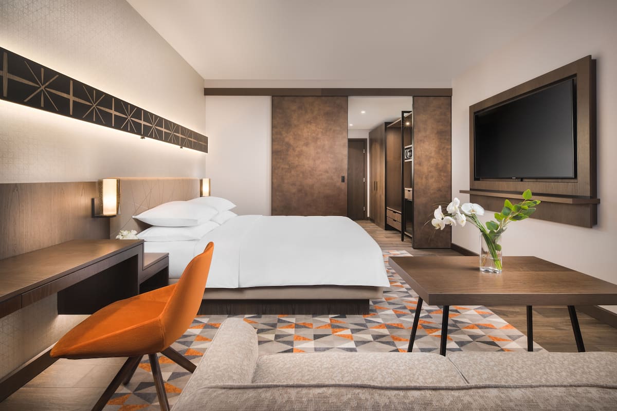 Ein modernes Hotelzimmer mit einem Bett, einem Schreibtisch, einem Stuhl, einem Fernseher und einer Vase mit Blumen.