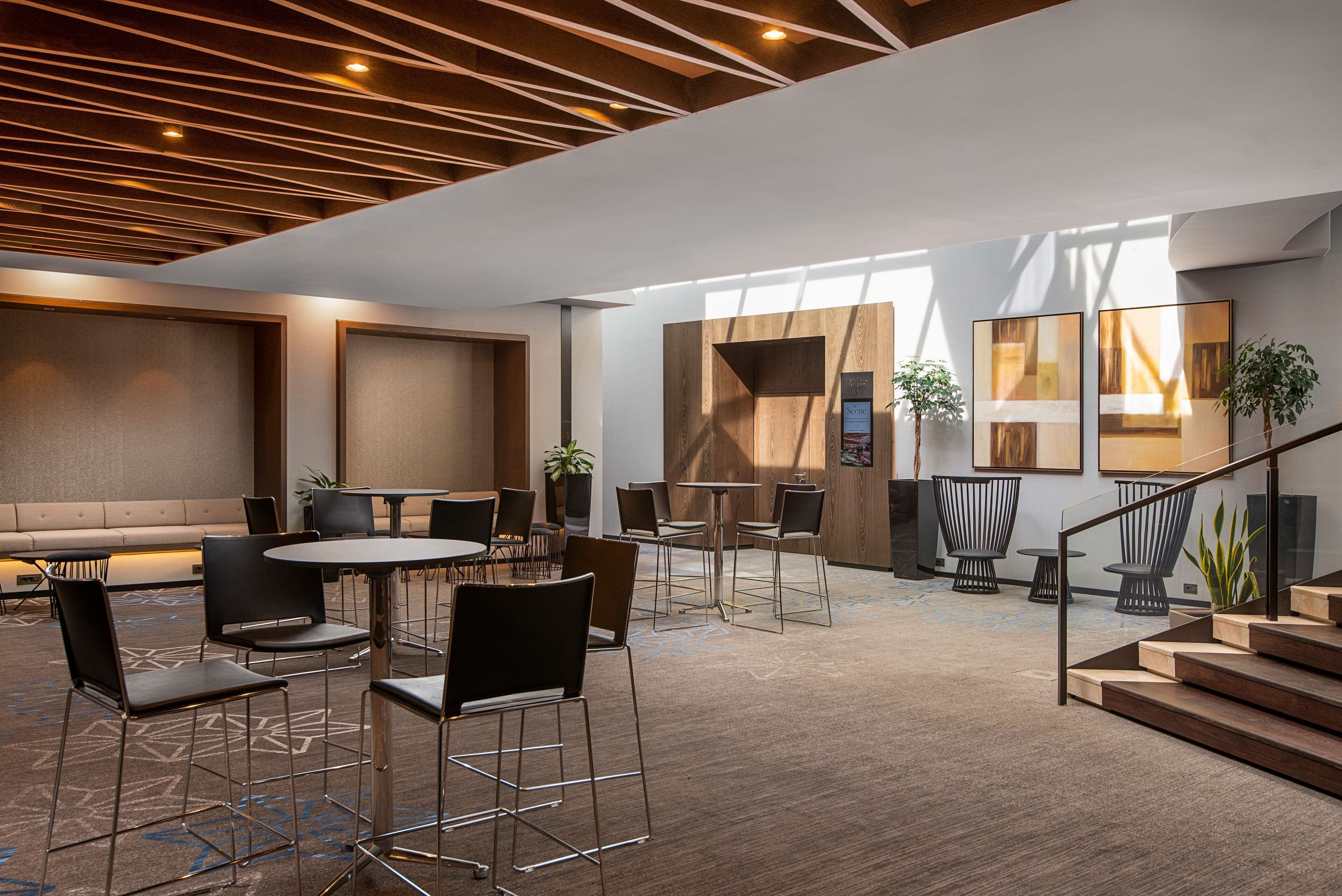 A modern hotel lobby with a seating area, tables, and a staircase.