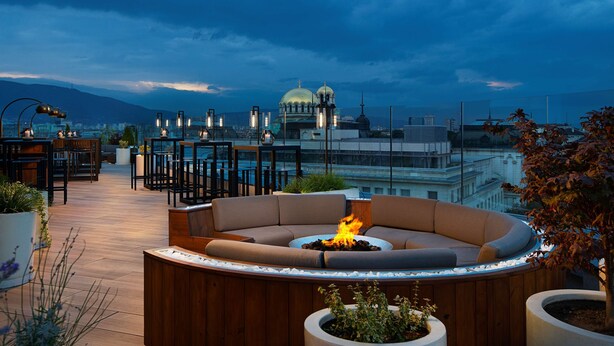 A rooftop lounge with a circular seating area, a fire pit, and a view of a cityscape and a mosque in the background. - Hyatt Regency Sofia (Sofia)