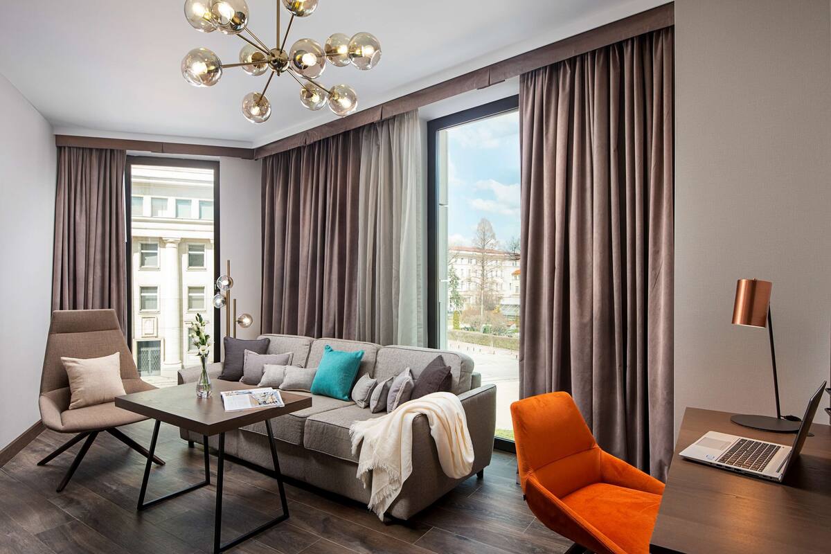 Ein modernes Wohnzimmer mit einer Couch, Sesseln, einem Couchtisch und einem Schreibtisch mit einem Laptop.