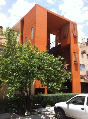 Un edificio moderno con un diseño arquitectónico distintivo, que presenta una fachada anaranjada destacada y un balcón con celosías.