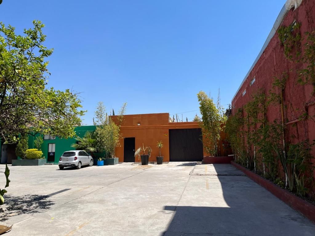 Un estacionamiento con un coche blanco, un edificio con una puerta de garaje oscura y una pared roja con plantas trepadoras.